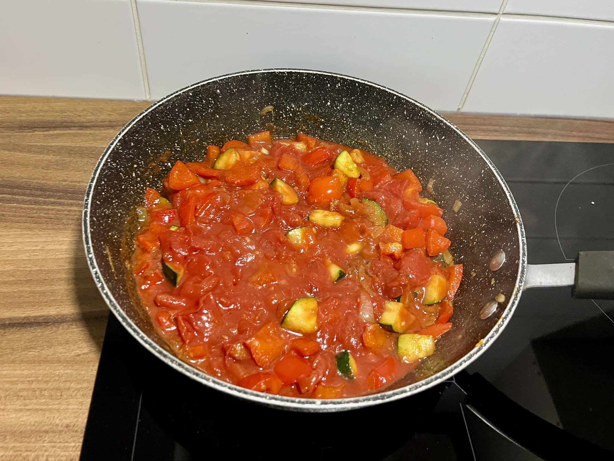 Chopped tomatoes added to a pan with the onion, garlic, courgette, and bell pepper.