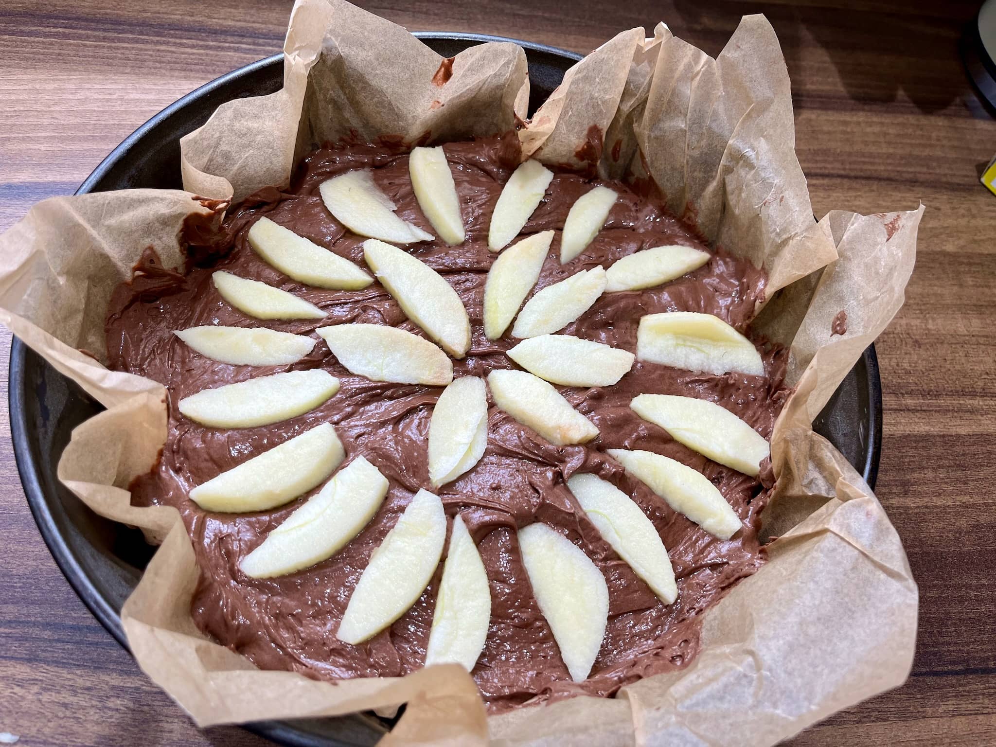 Chocolate cake mixture in a baking tray with apple slices in a pattern