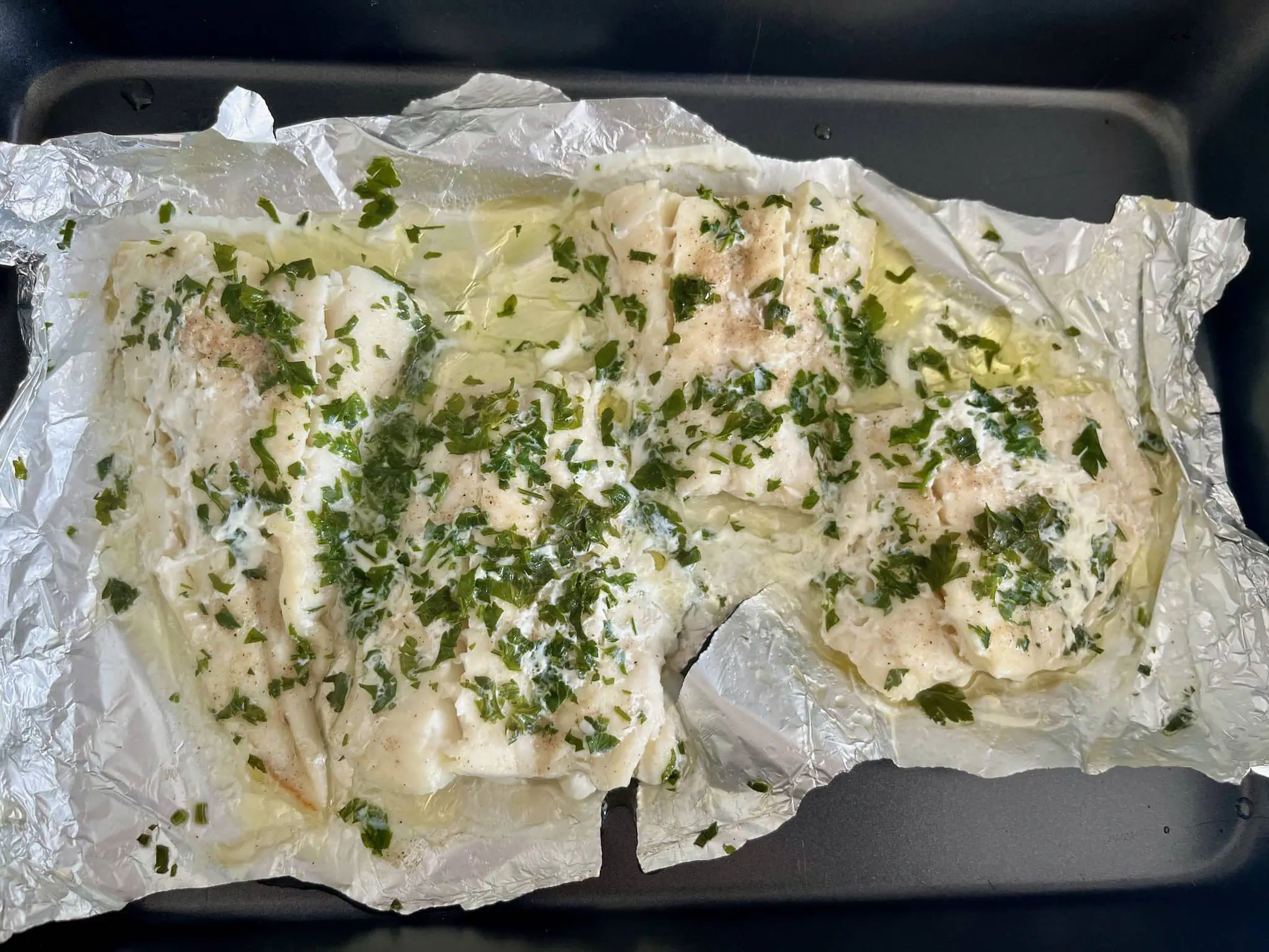 Prosta ryba pieczona w piekarniku, nadal na blasze, świeżo wyjęta z piekarnika.