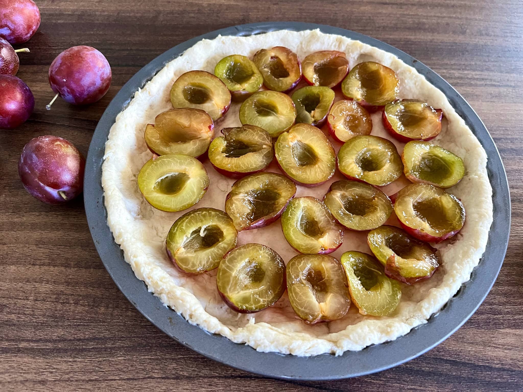 Neatly arranged plum halves on top of tart dough in a tray
