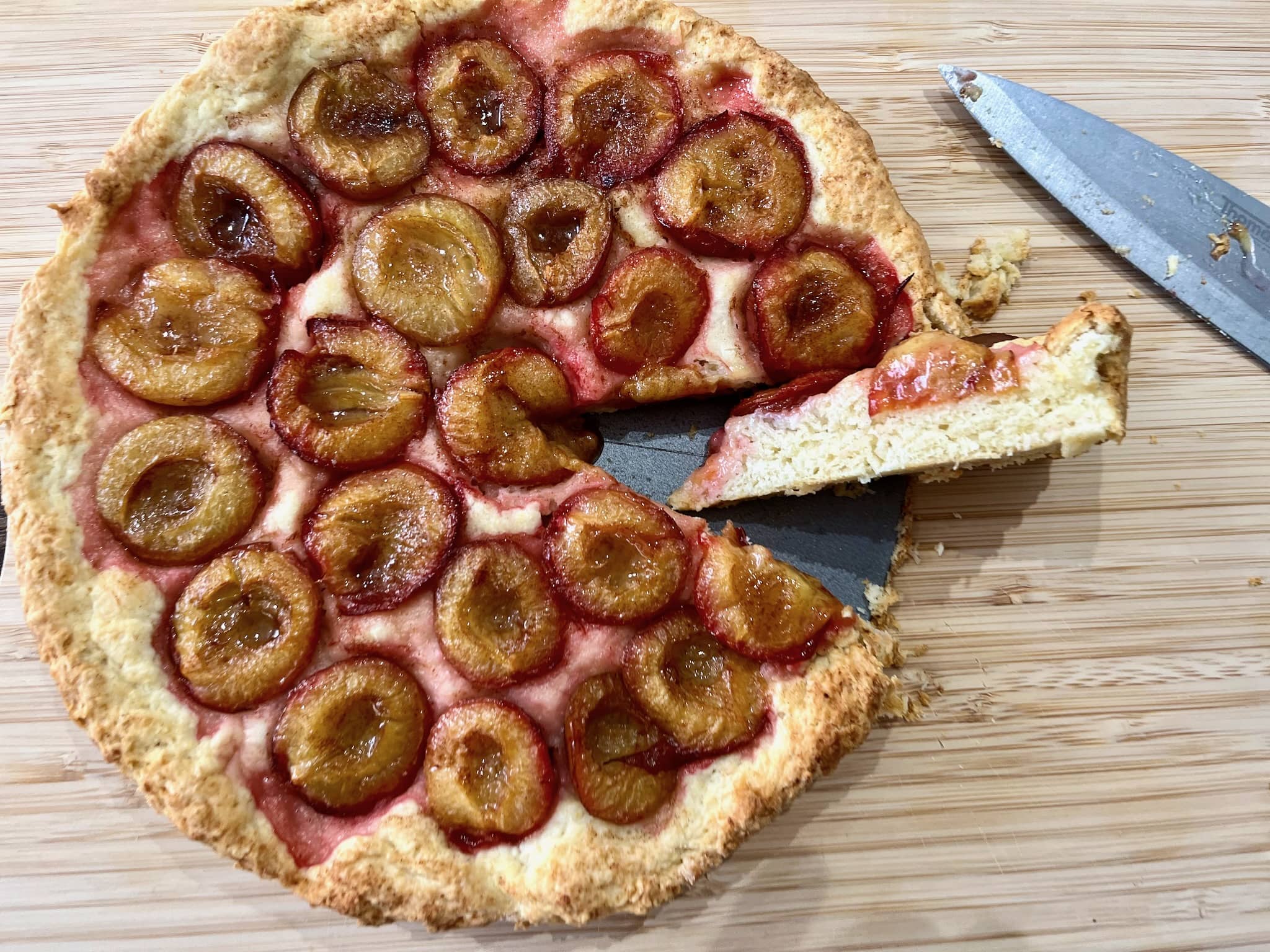 Baked plum tart taken out from the tin crust with a sliced piece