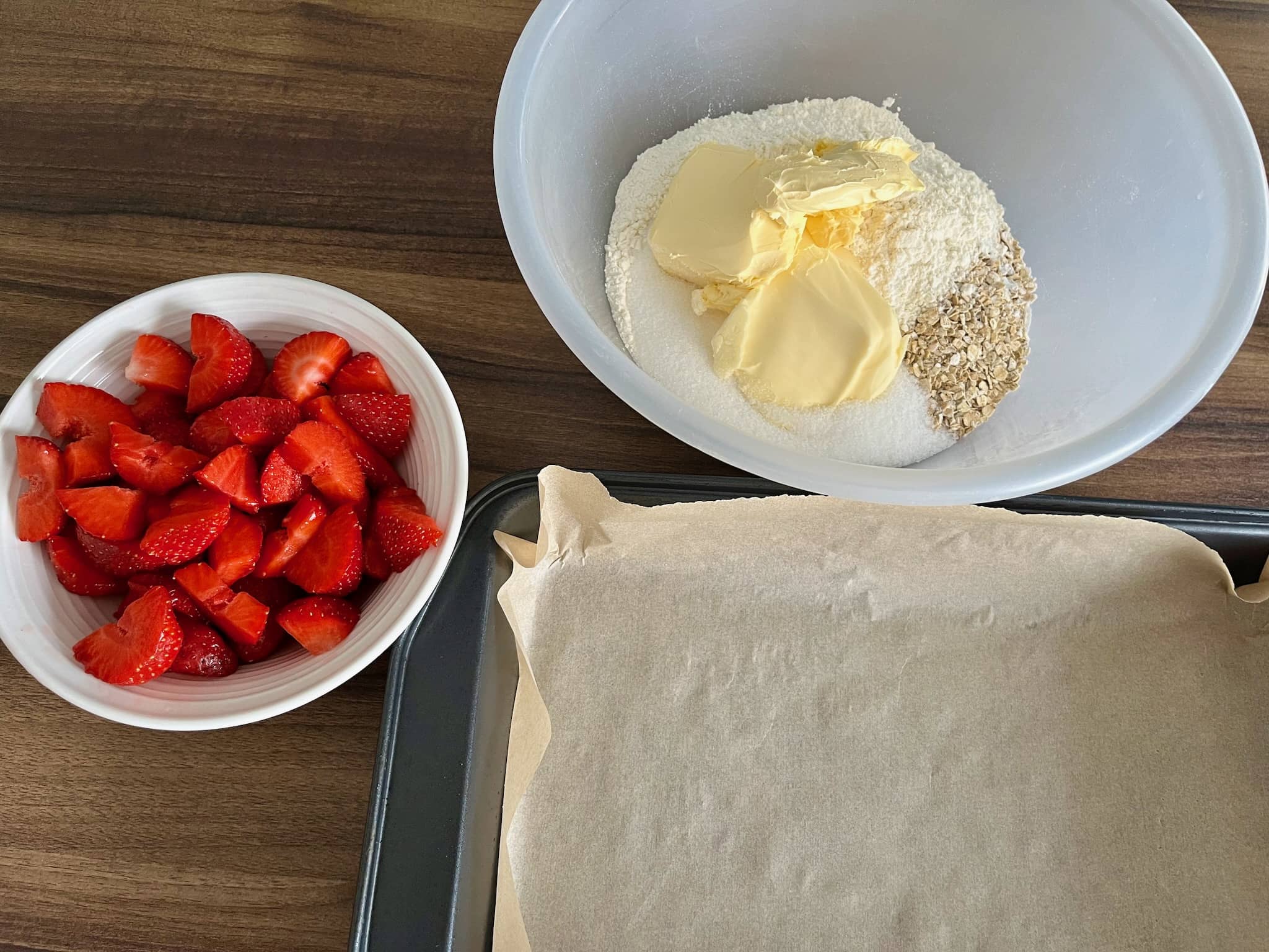 Strawberries cut, tray lined with baking paper and other ingredients in a bowl