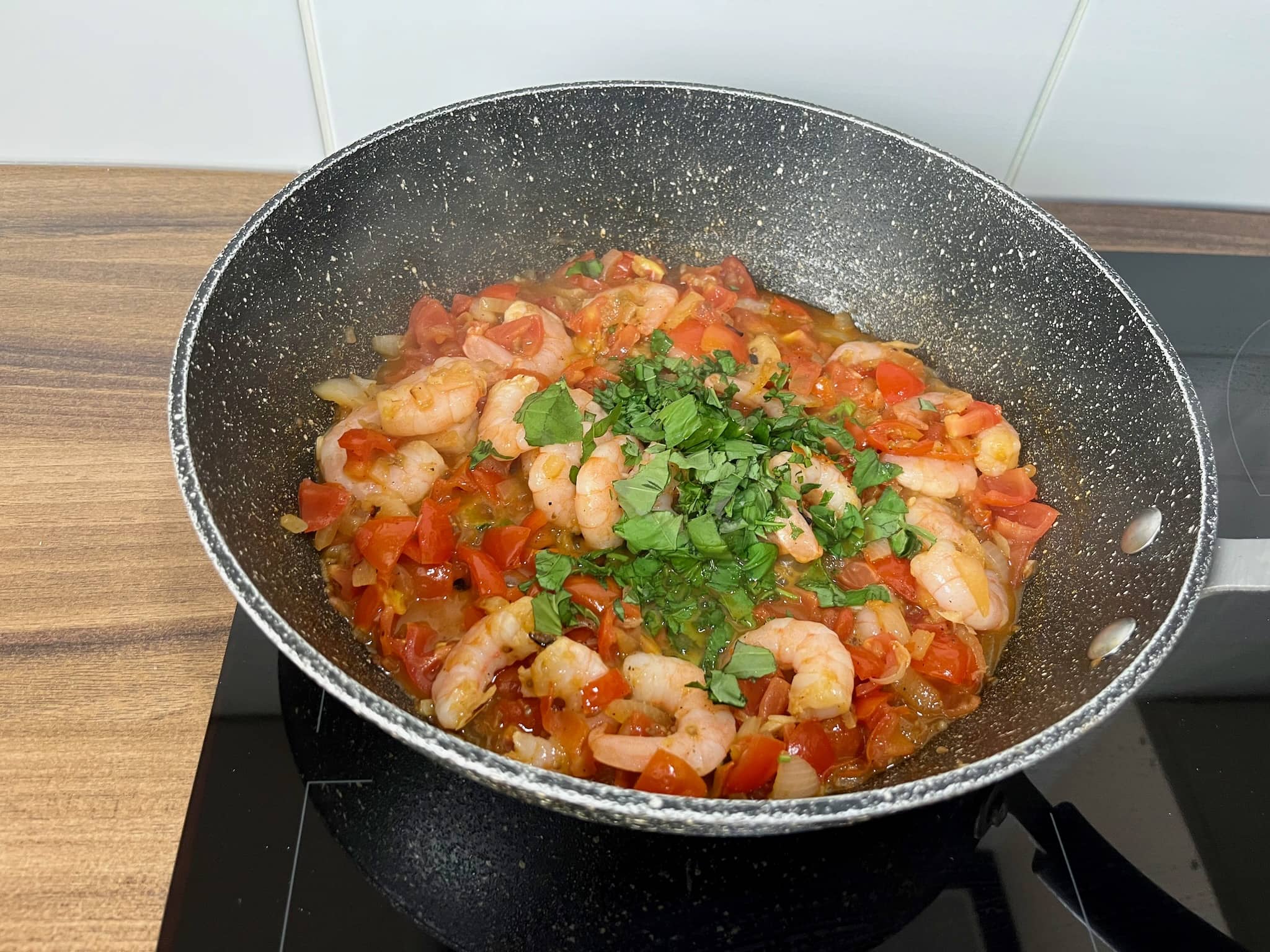 Tomatoes, onion and garlic frying in a pan with added prawns and basil