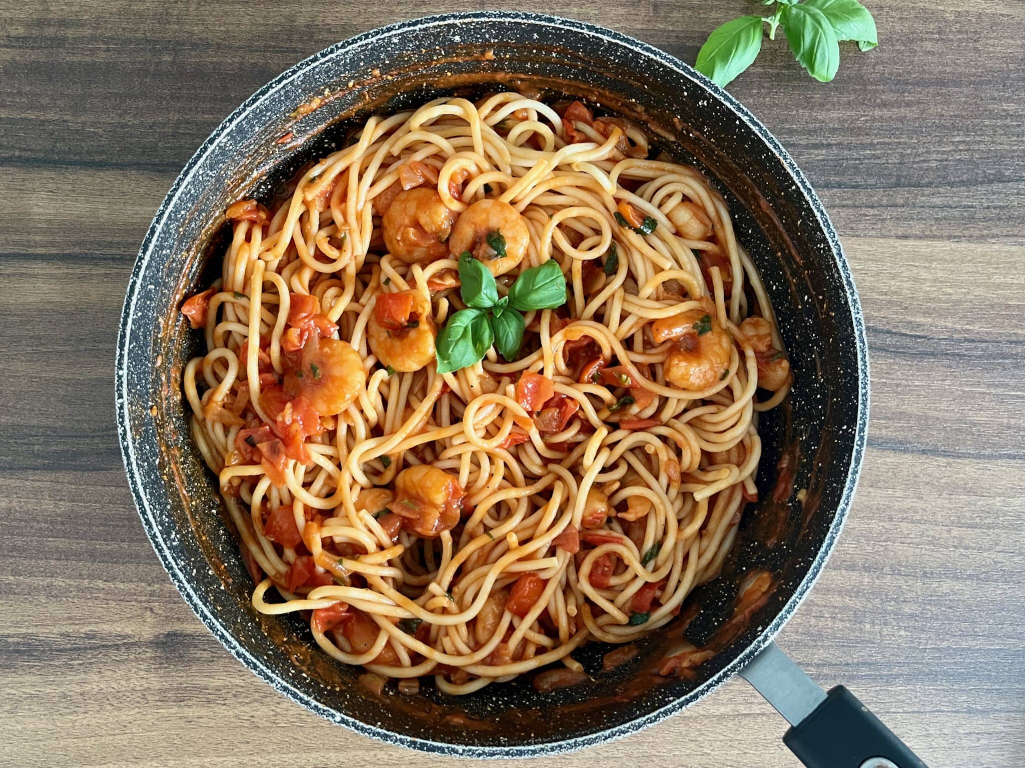 Pasta mixed with tomatoes, basil and prawns in a pan