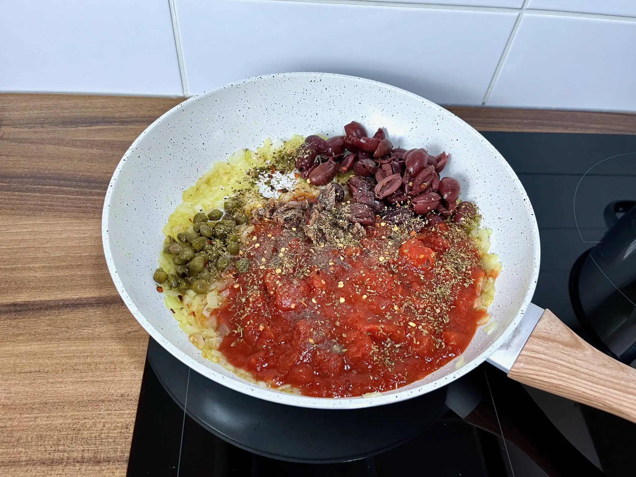 Dodanie pomidorów, kaparów, anchois, oliwek i przypraw na patelnię