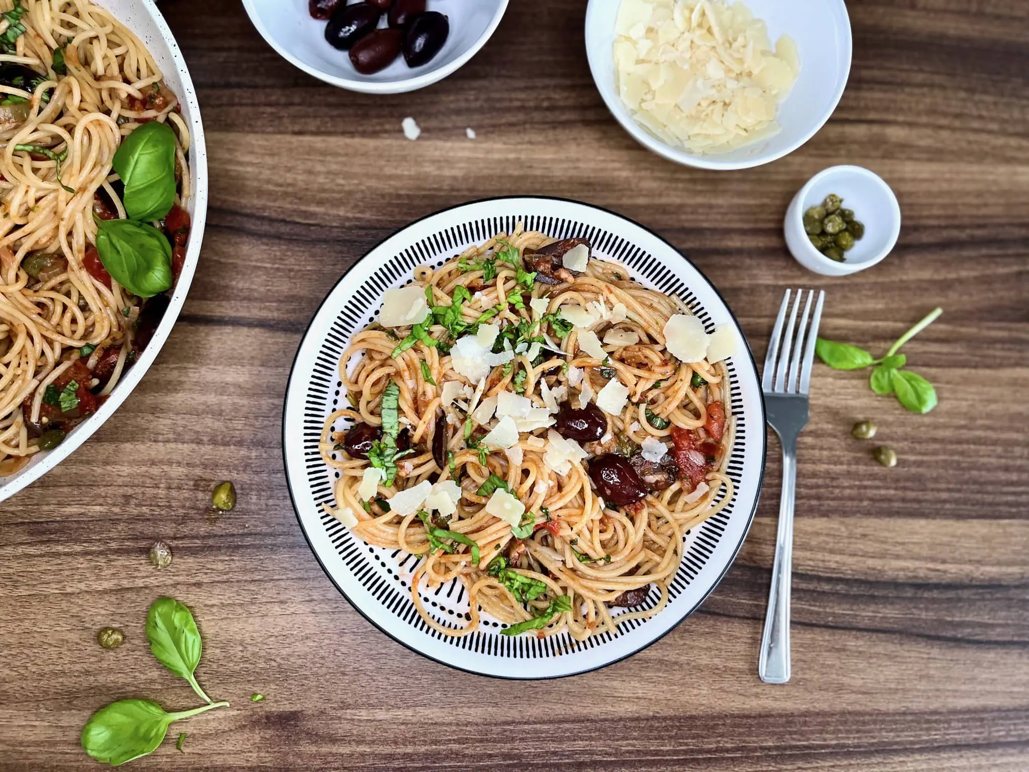 Porcja Spaghetti Puttanesca, udekorowana startym serem Parmezan i liśćmi bazylii