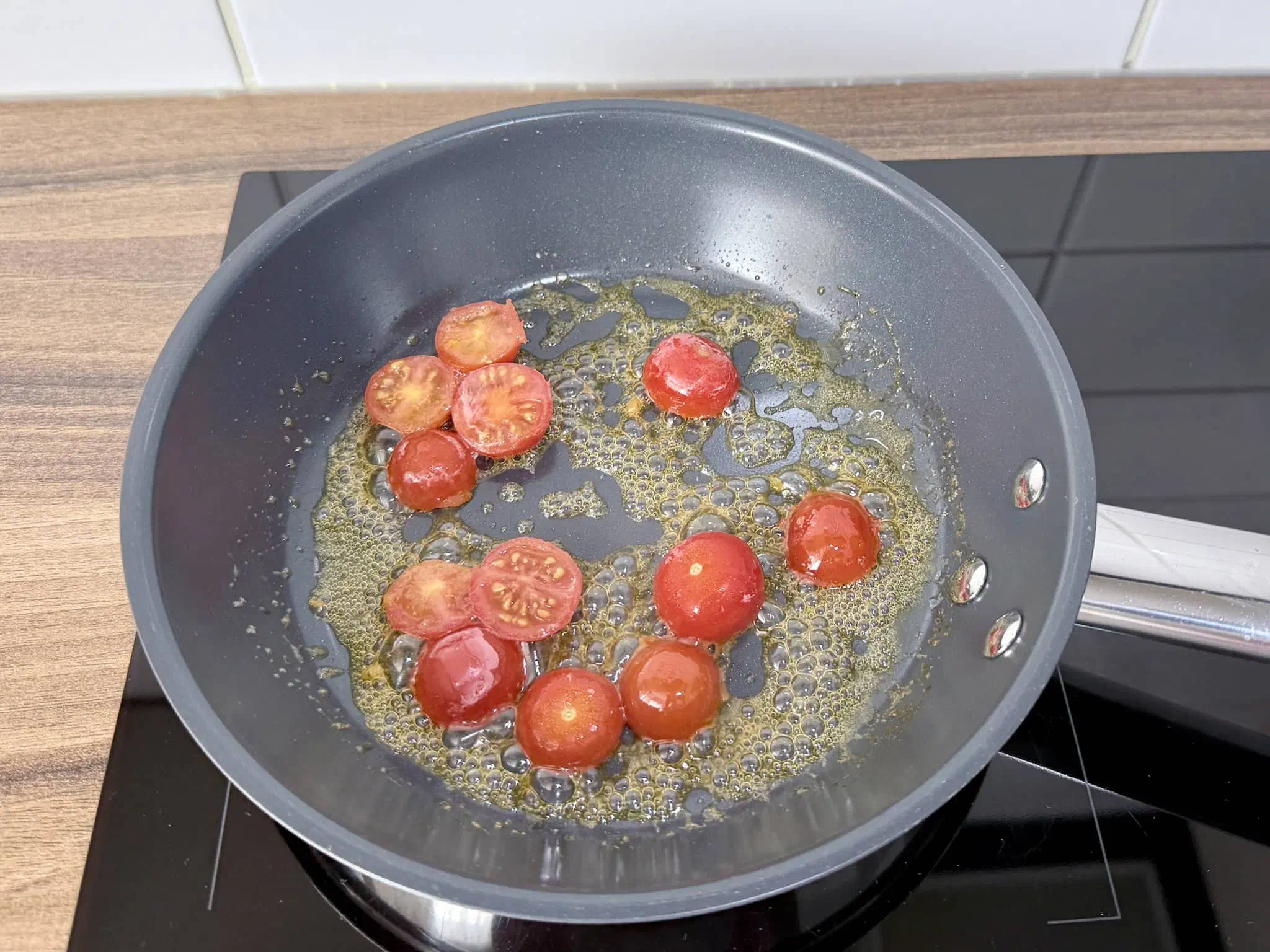 Tomatoes frying in a pan with a teaspoon of butter