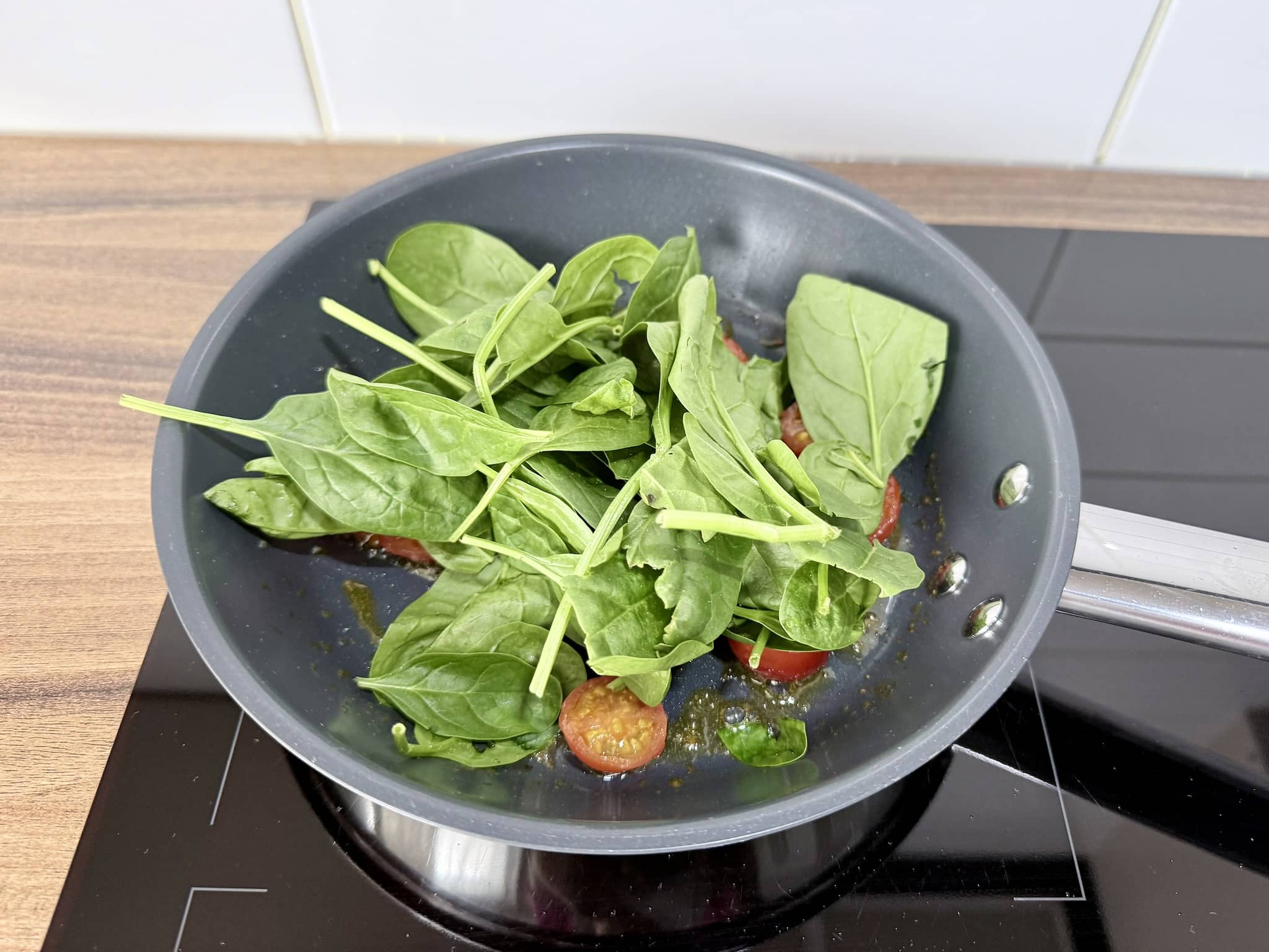 Spinach frying in a pan with tomatoes and butter