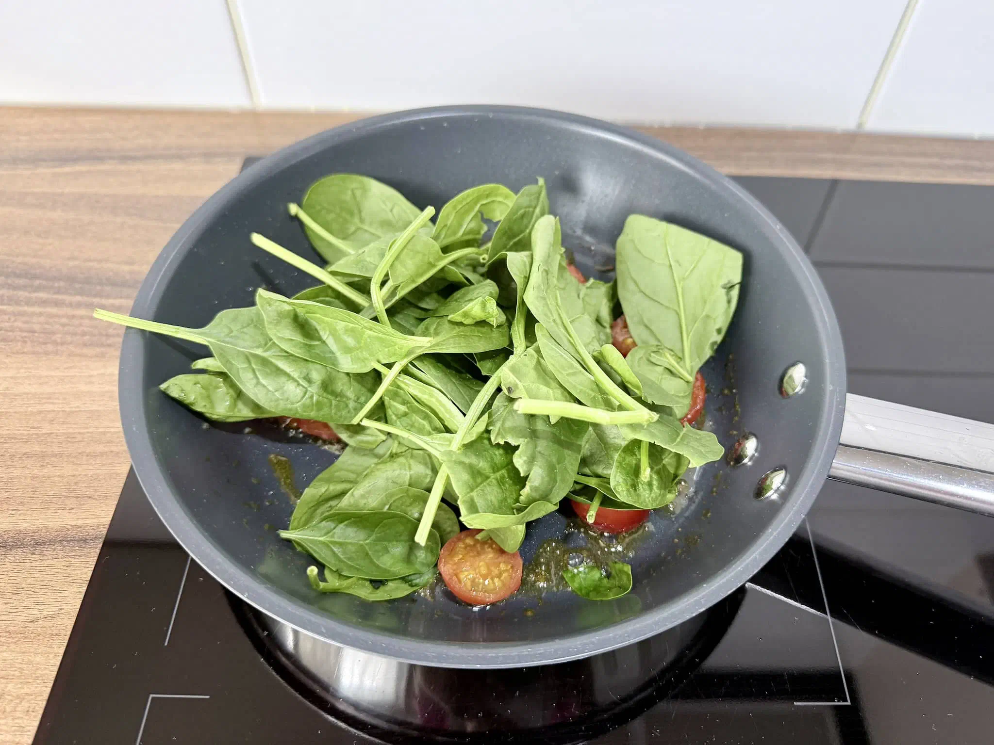 Spinach frying in a pan with tomatoes and butter