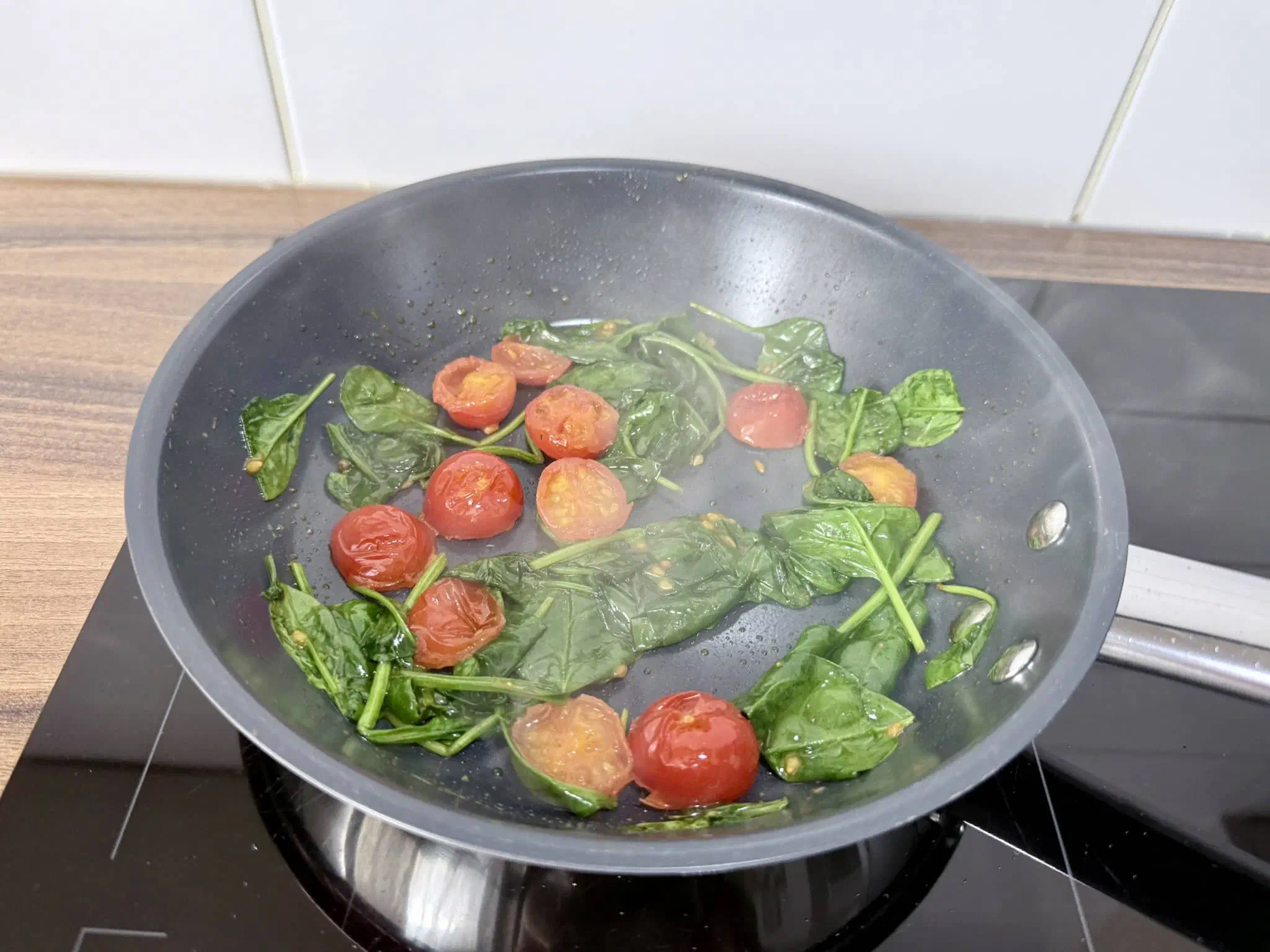 Nicely fried and wilted spinach with mini tomatoes in a pan