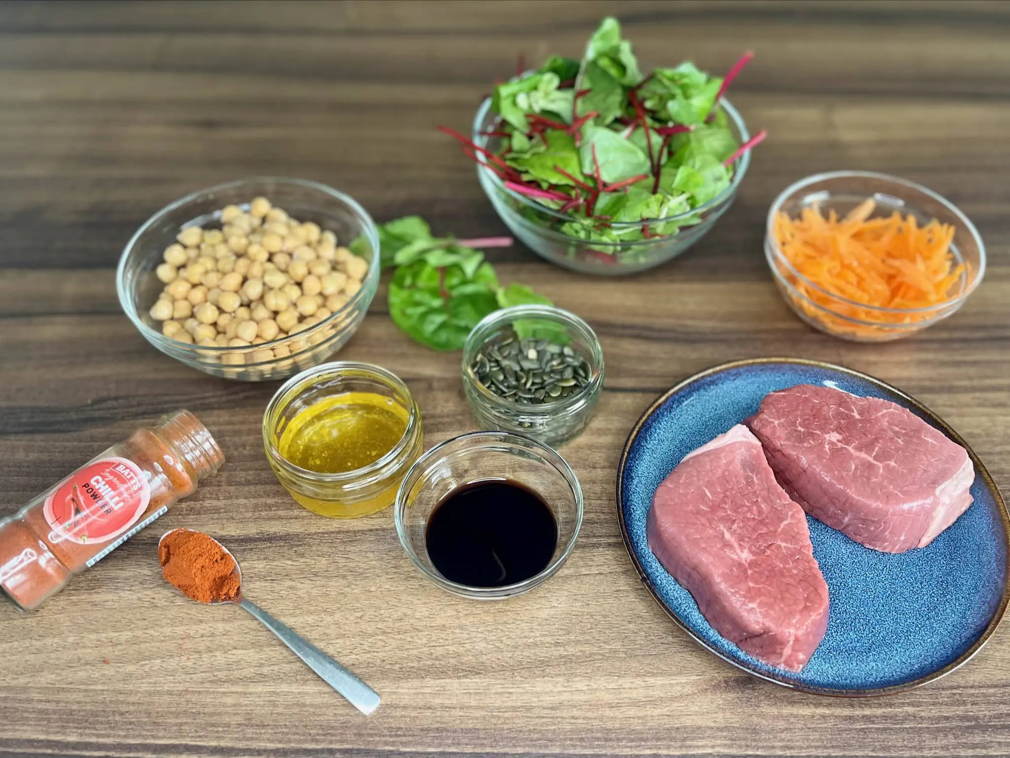 Wszystkie składniki są przygotowane na stole, gotowe do przyrządzenia sałatki superfood ze stekiem i ciecierzycą
