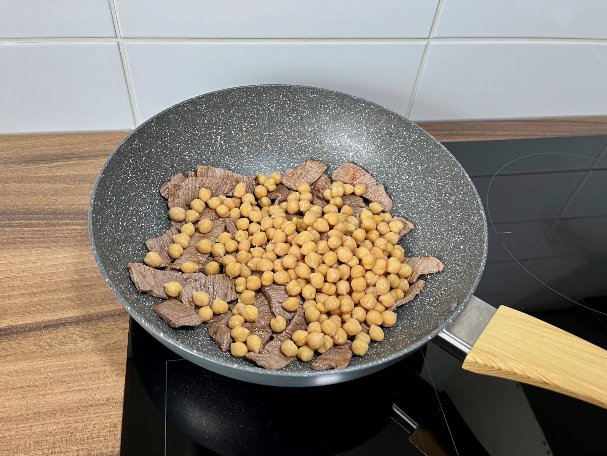 Cooked steak meat slices with chickpeas on top, in a large skillet
