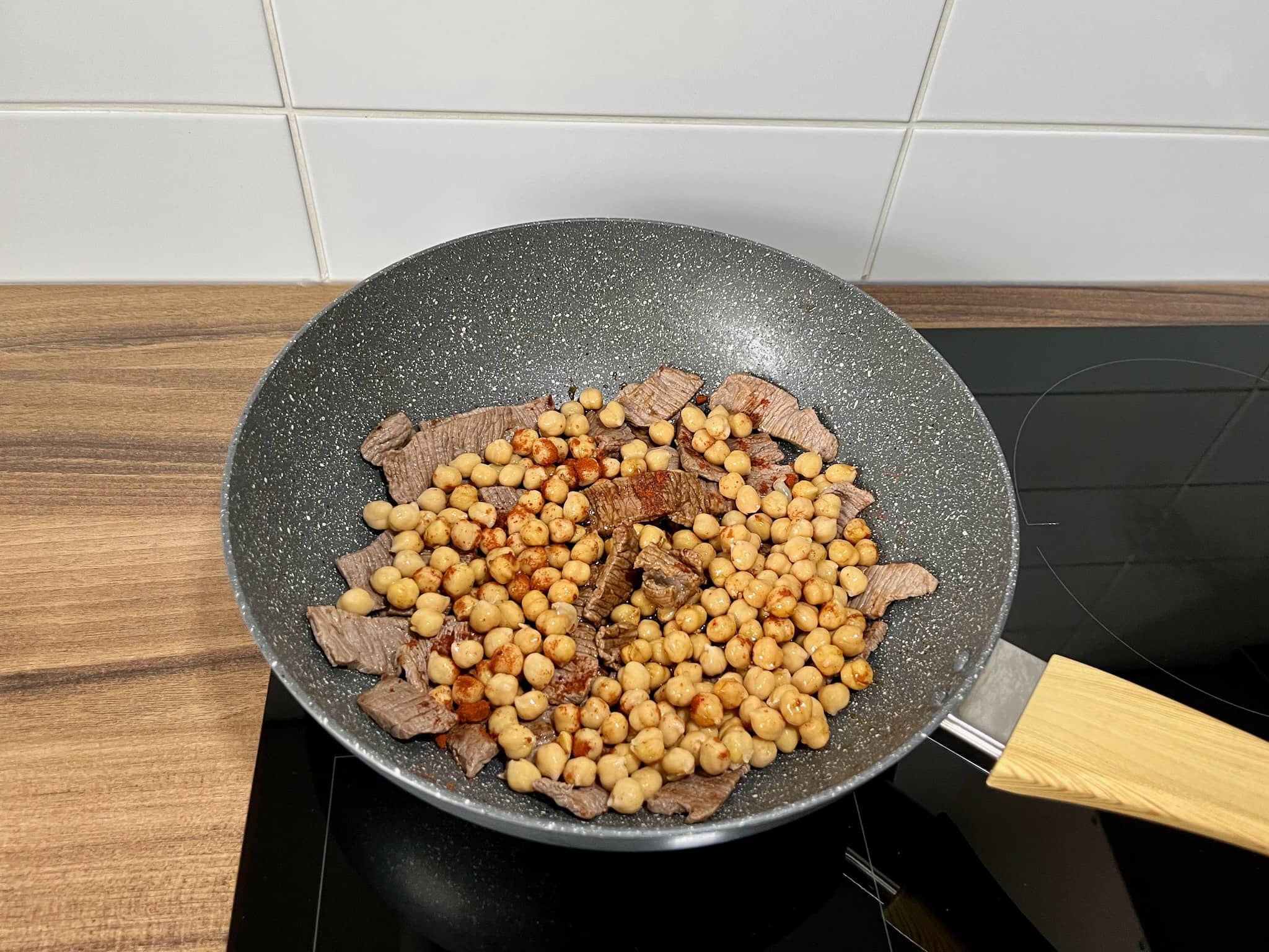 A large skillet filled with cooked steak meat slices, chickpeas, and spices