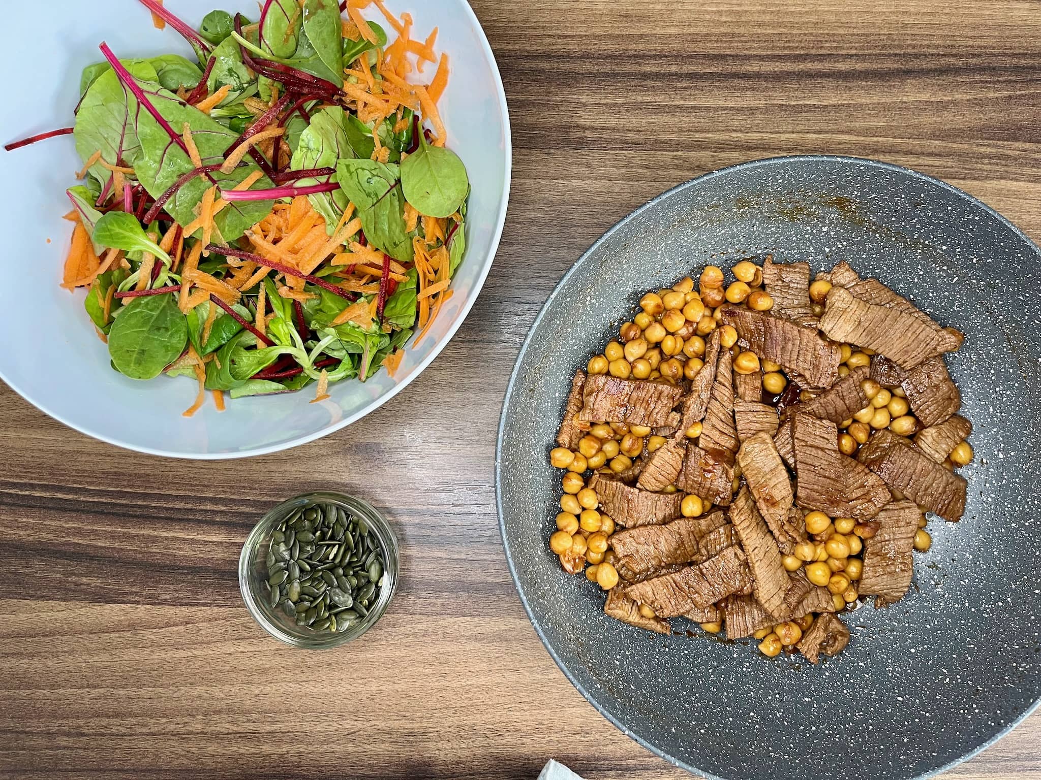 A bowl of mixed salad with steak meat and chickpeas on the side, and a small bowl of pumpkin seeds