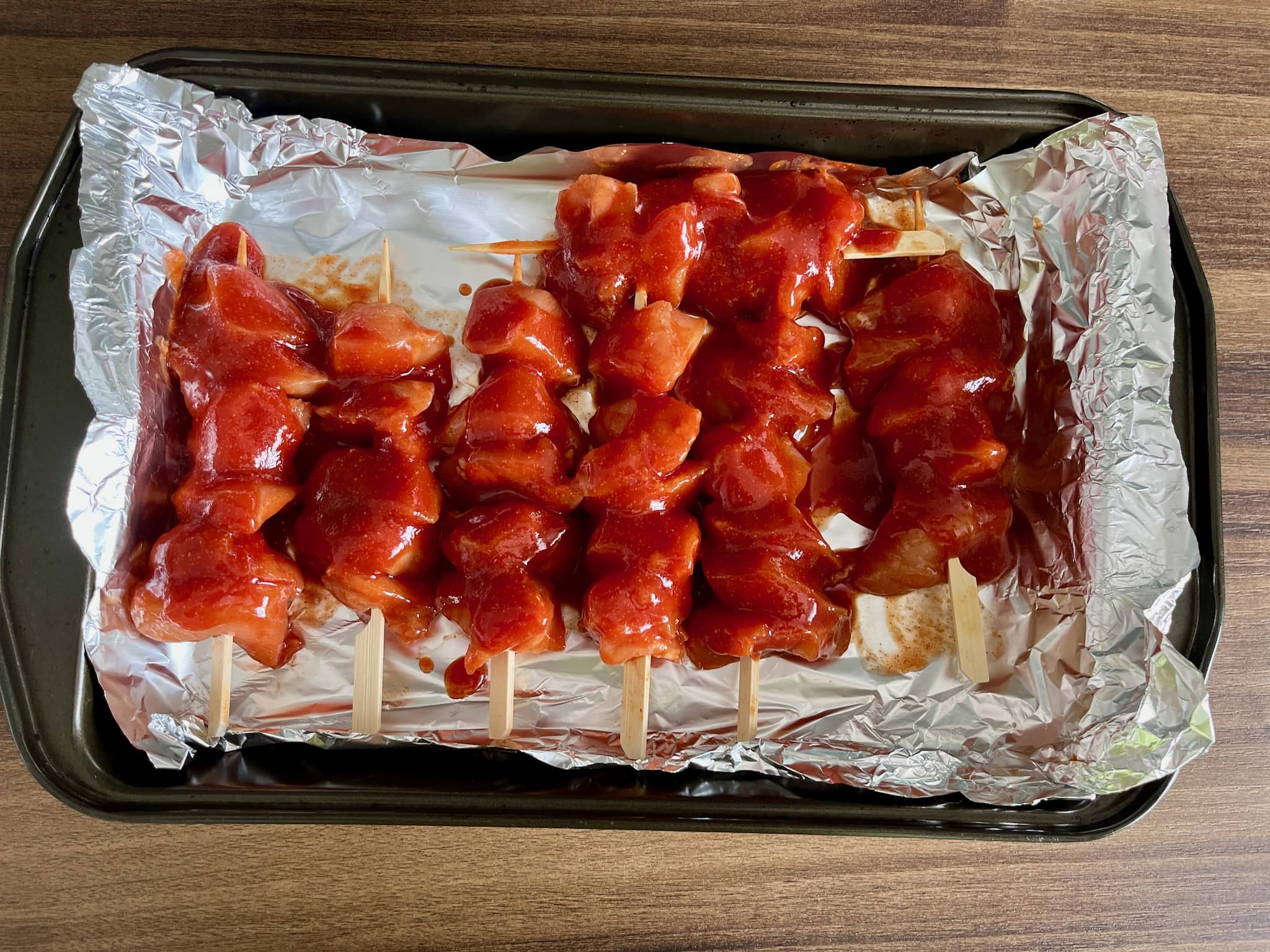 Impaled chicken breast cubes on skewers covered with sticky sauce in a baking tray