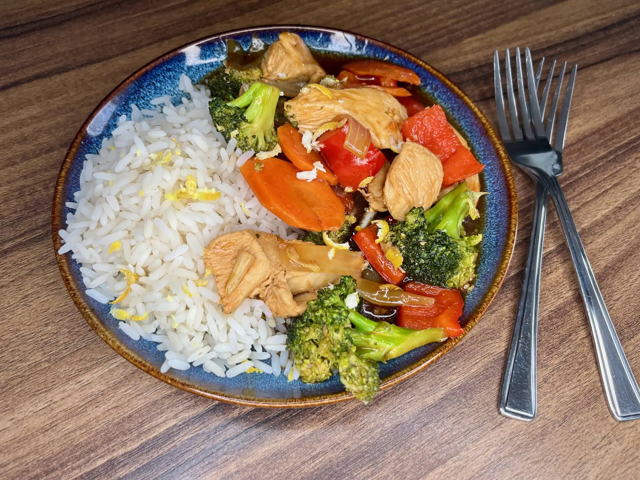 Kurczak cytrynowy stir-fry na talerzu z ryżem i posypany skórką z cytryny