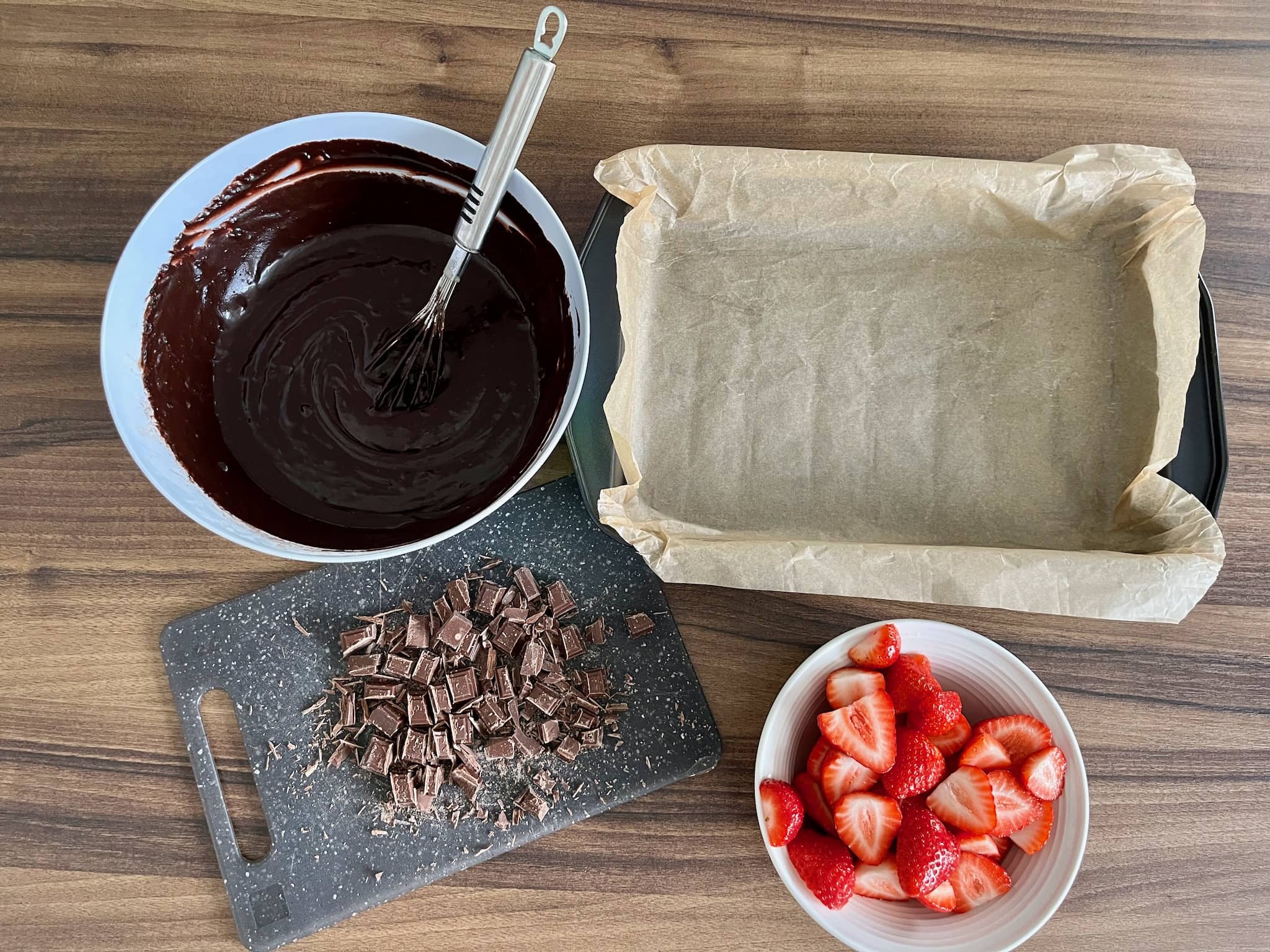 Brownie mix in a bowl, chocolate chopped, baking tray lined and strawberry halved
