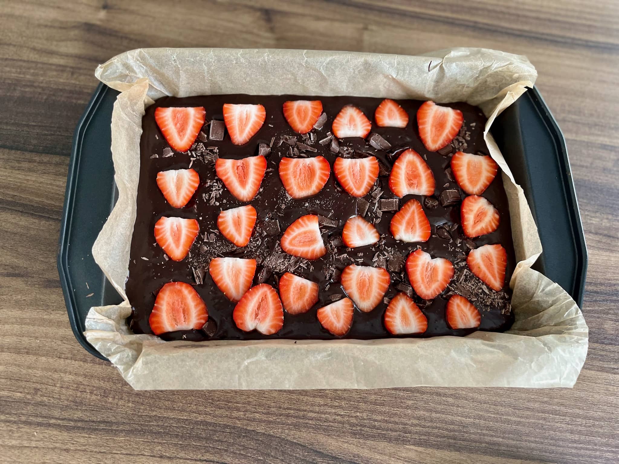 Brownie mix in a baking tray with chopped chocolate and strawberries, ready to bake
