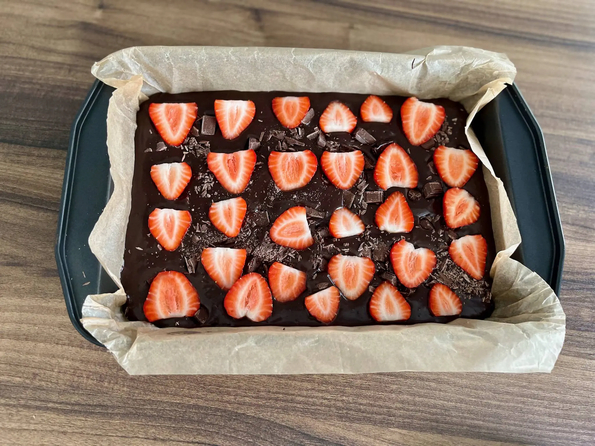Masa na brownie w blaszce, posypana czekoladą i truskawkami, gotowa do pieczenia