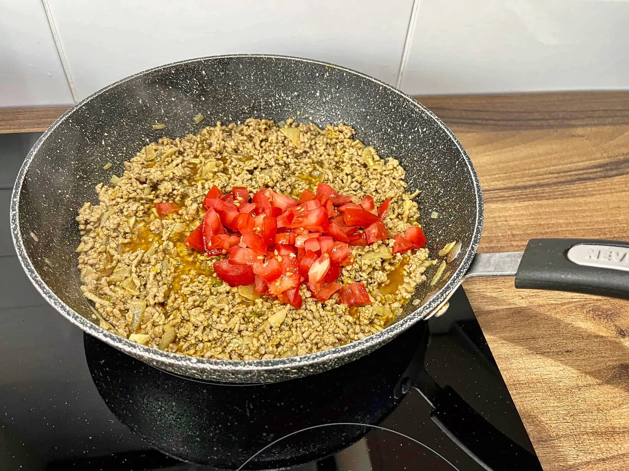 Meat with onion and garlic in a pan and freshly chopped tomato on the top