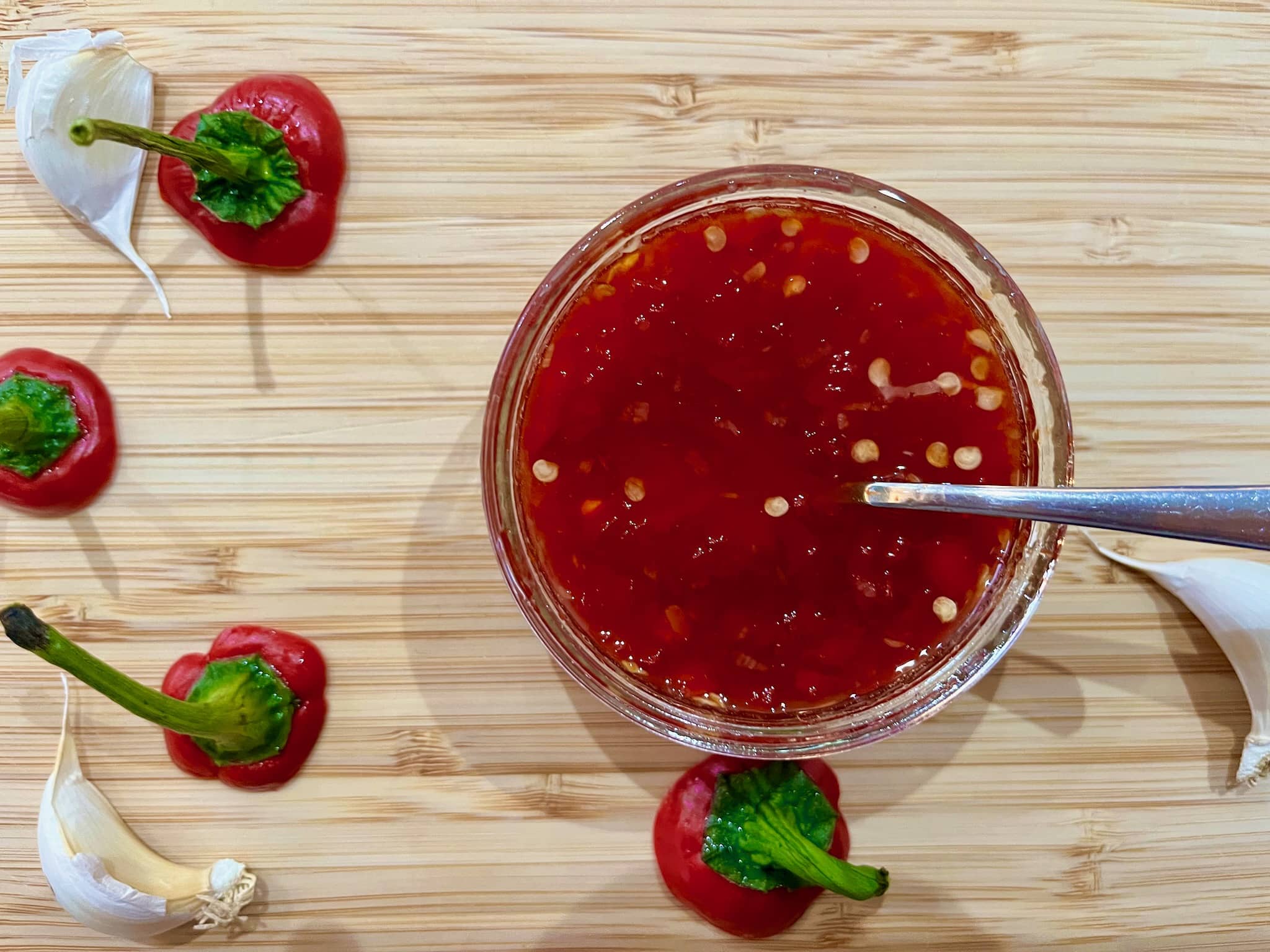 Sweet Chilli Sauce in a sauce glass with a spoon inside and decorations on the chopping board.