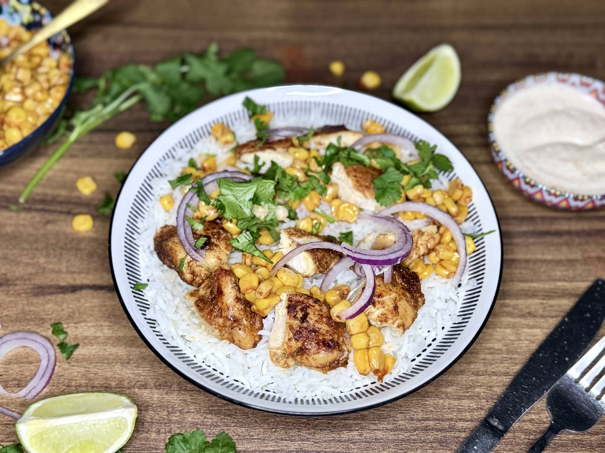 A rice bowl with sweetcorn and sliced chicken, garnished with red onion and fresh coriander