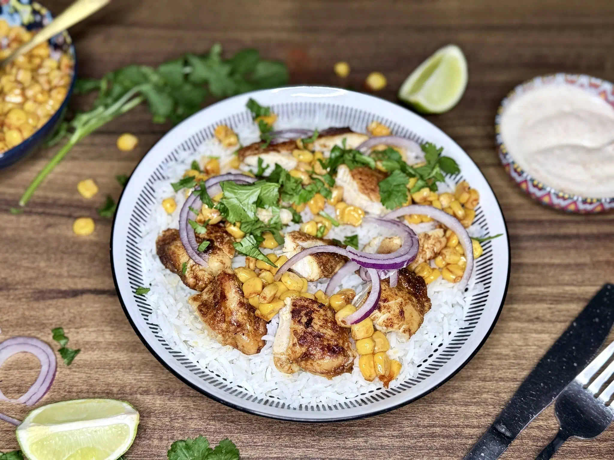 A rice bowl with sweetcorn and sliced chicken, garnished with red onion and fresh coriander
