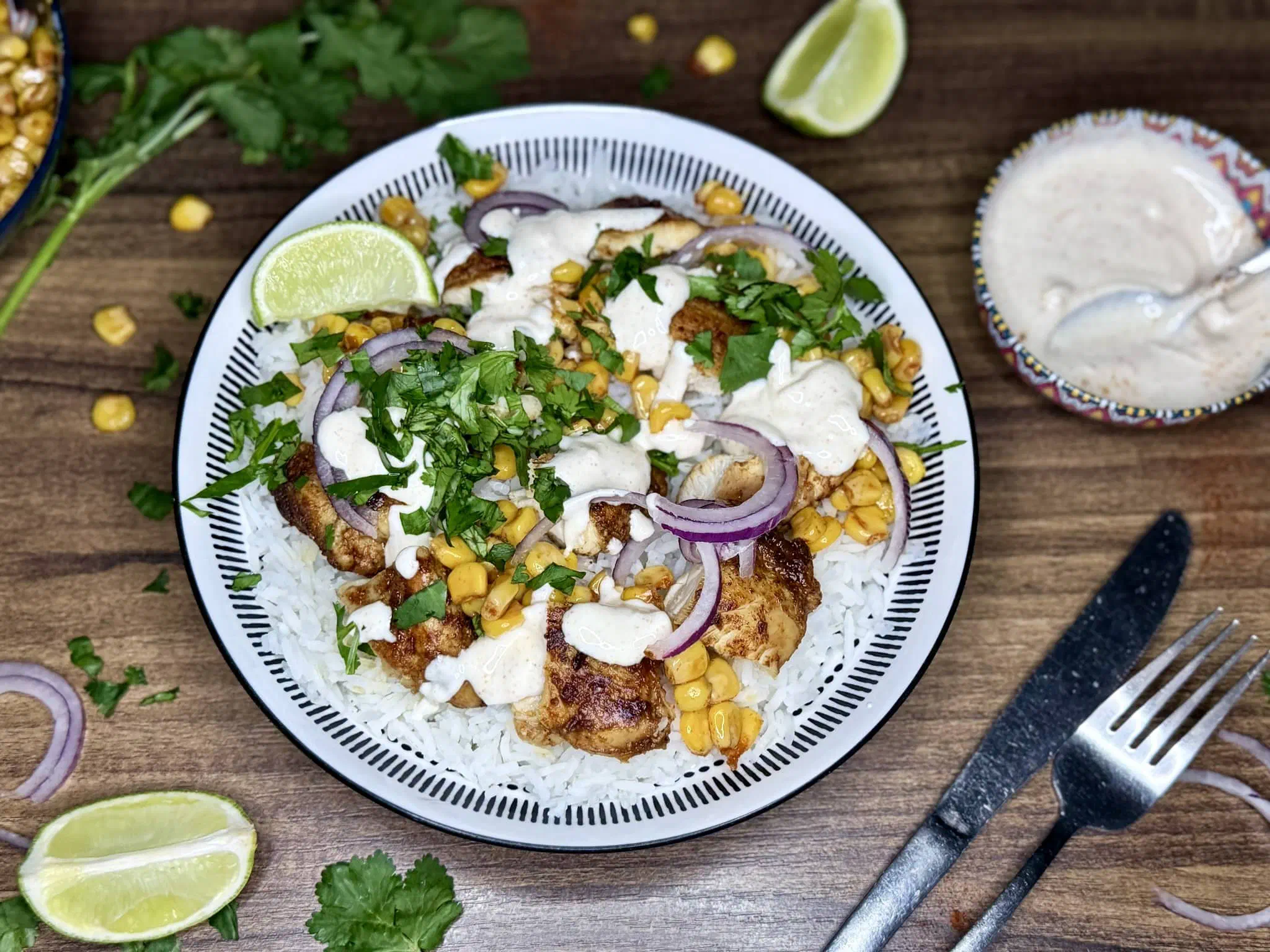 The finished Sweetcorn and Chicken Rice Bowl, drizzled with garlic sauce and served with lime