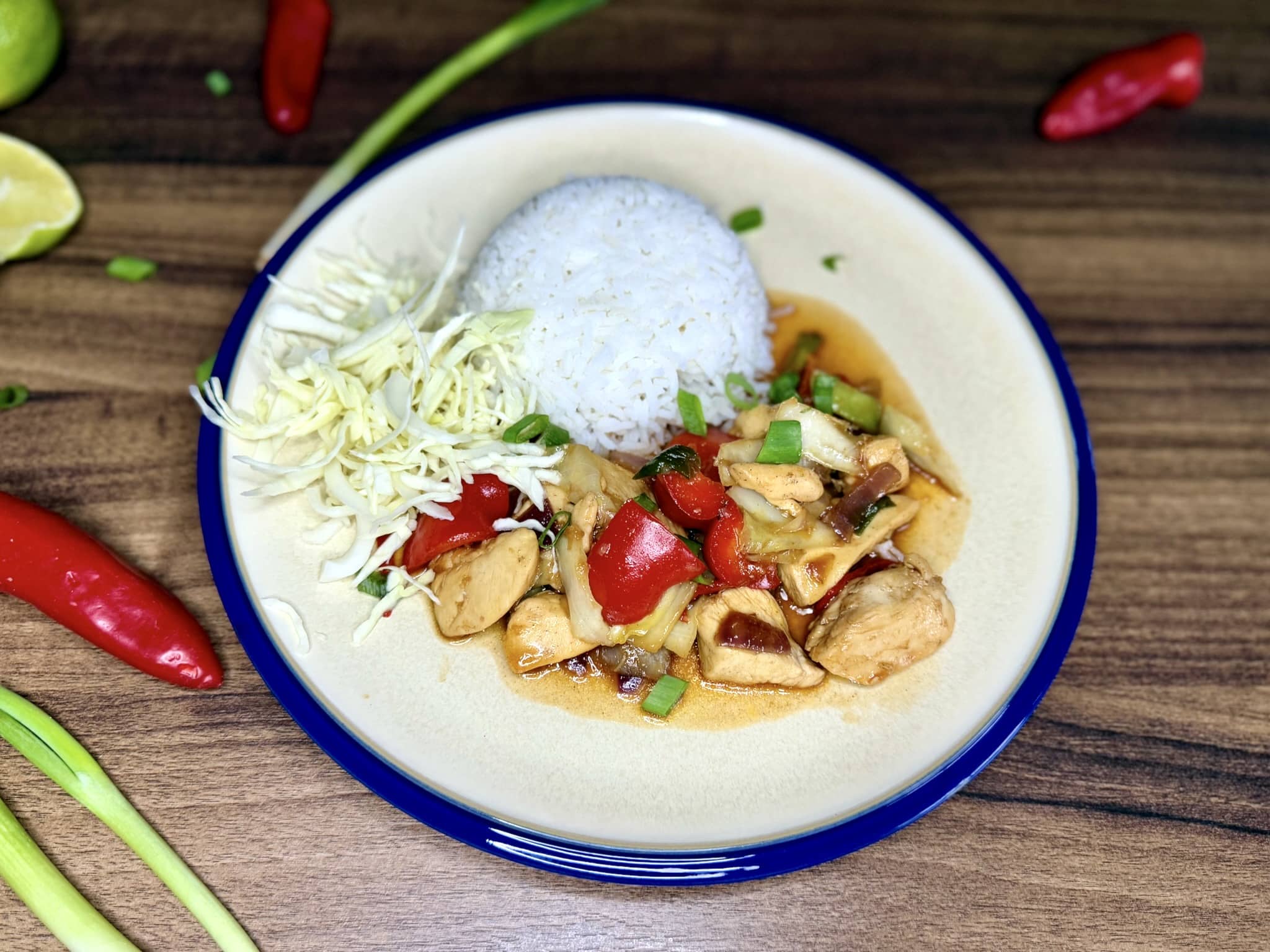 Thai Style Chicken served on a plate with rice, cabbage leaves, sprinkled with spring onion