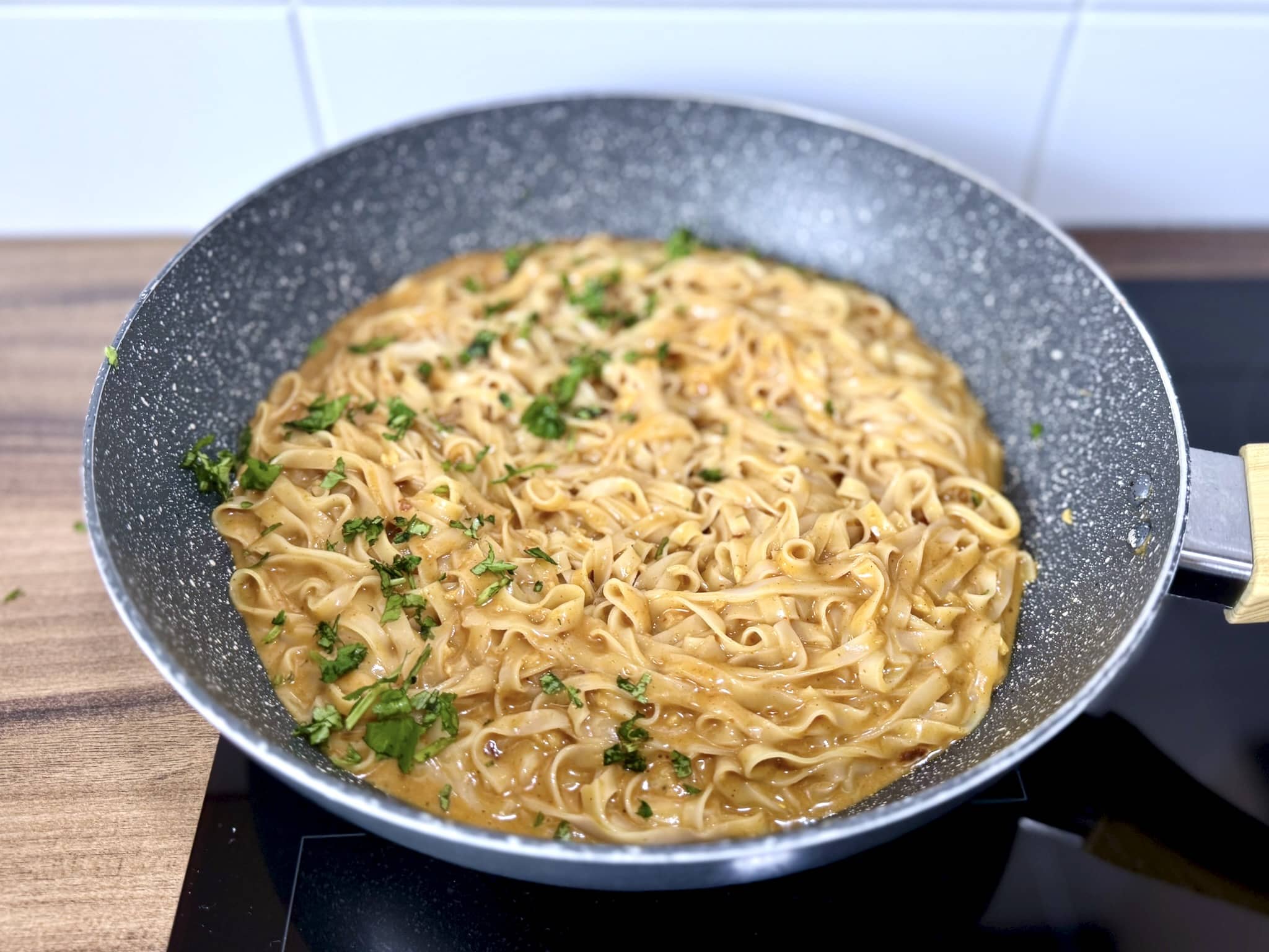 Gotowe tajskie curry z makaronem ryżowym wciąż na patelni, posypane świeżą kolendrą