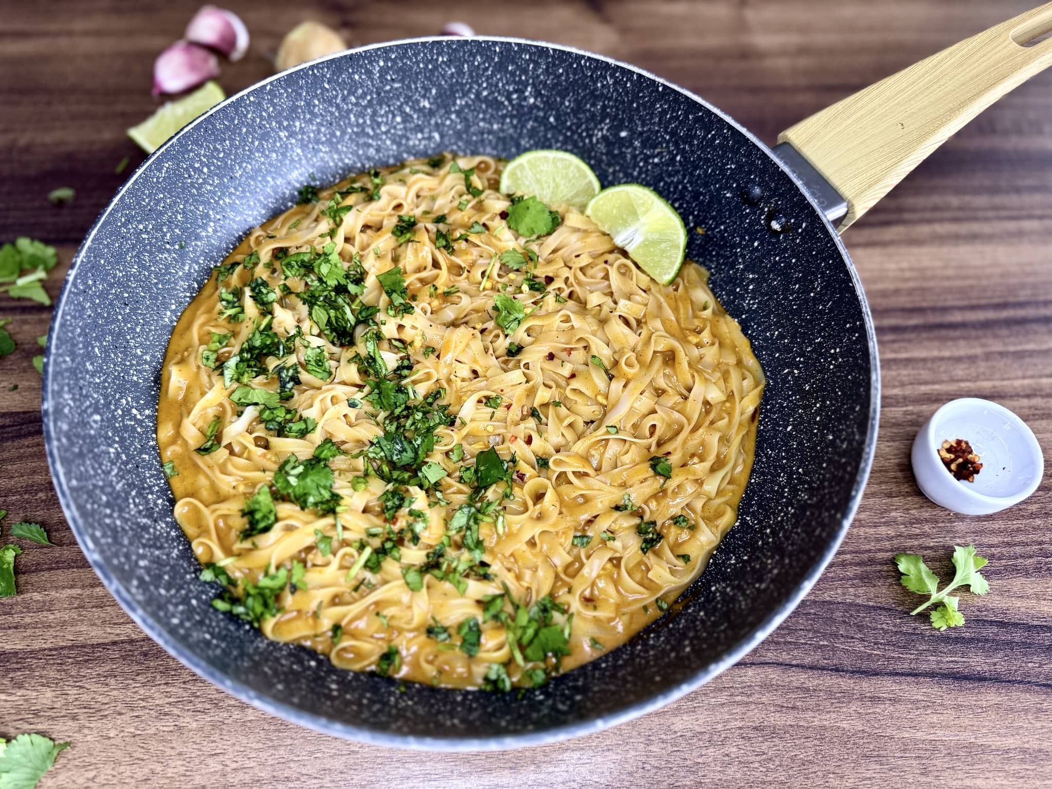 Tajskie curry z makaronem ryżowym w garnku ze świeżą kolendrą, płatkami chilli i dwoma kawałkami limonki