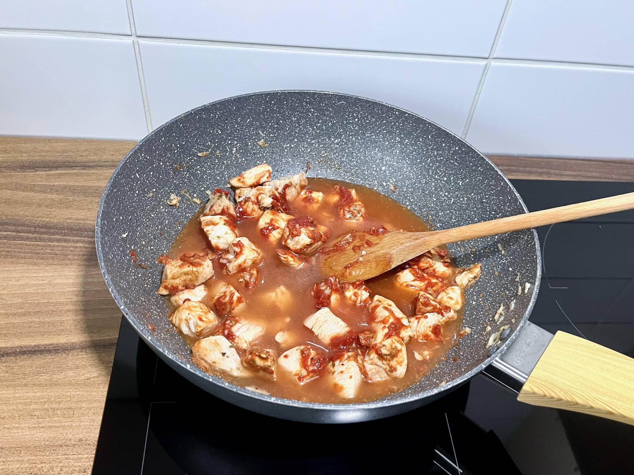 Chicken breasts are frying in a pan with tomato purée and water added