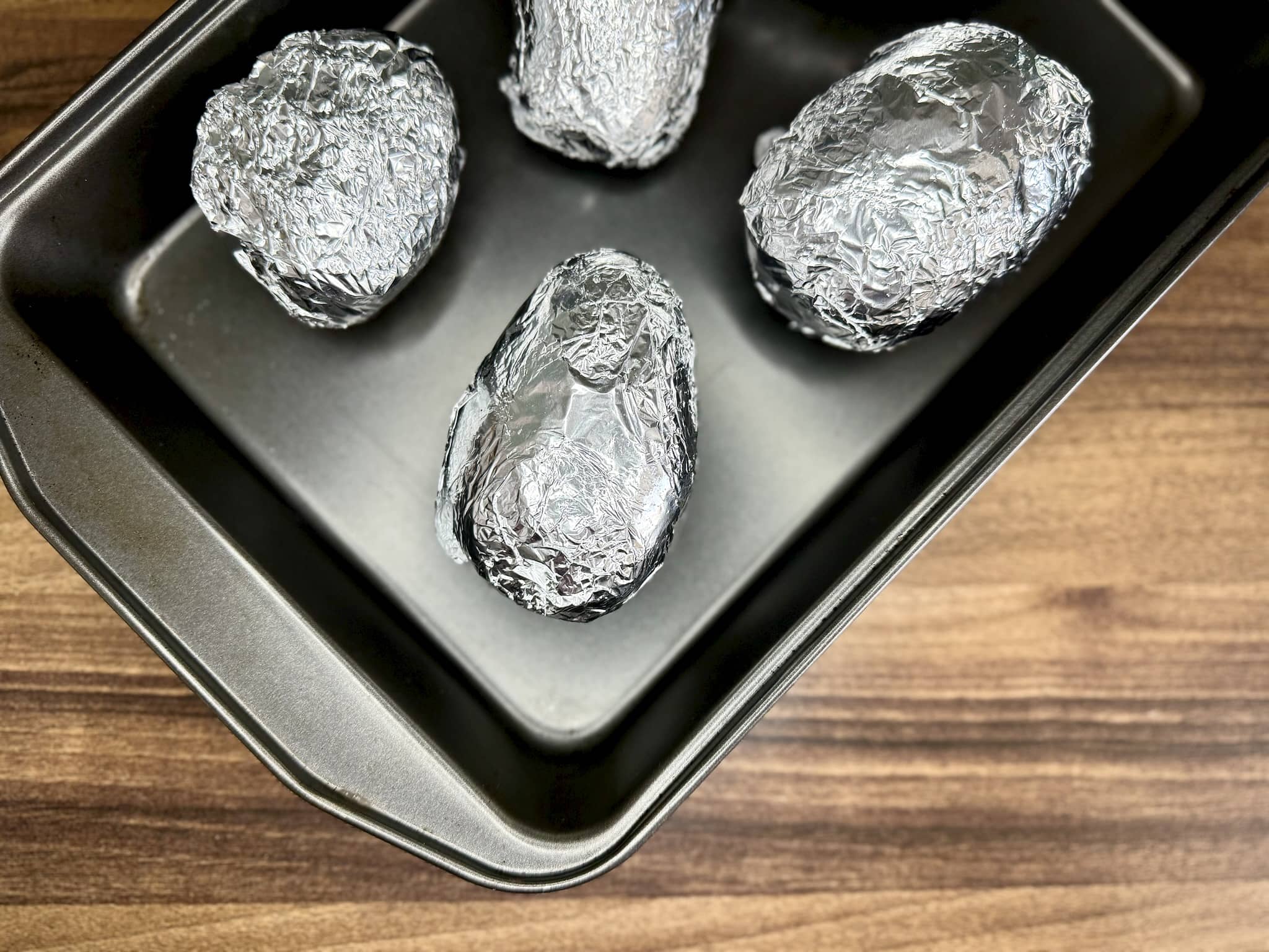 All potatoes wrapped in tin foil placed on a baking tray