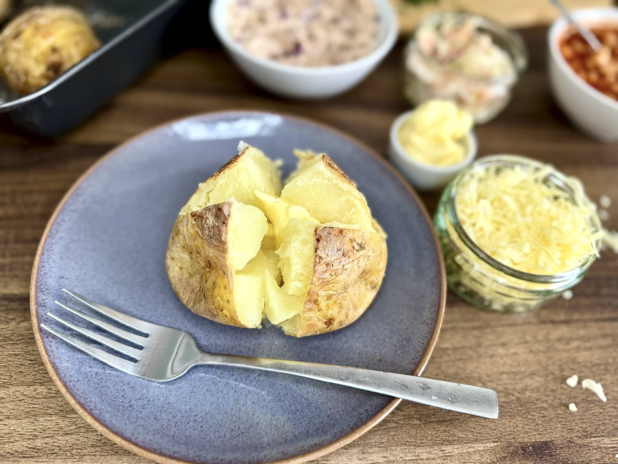 An opened baked potato on a plate with a piece of butter melting inside